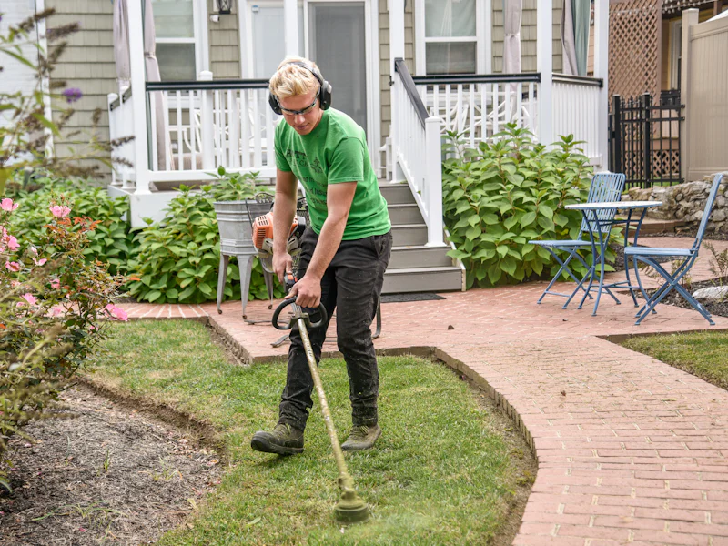A landscaper in a green shirt edging a lawn beside a brick walkway