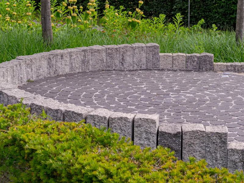 A round paver patio edged with a low stone block wall and green shrubs