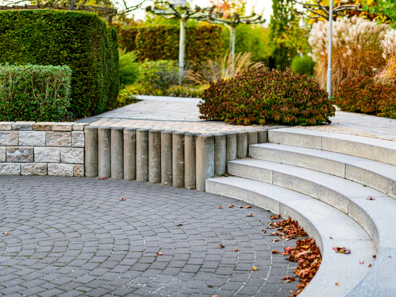 Curved stone steps leading down to a paver patio beside trimmed hedges